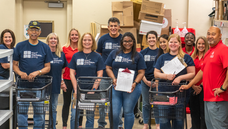 A group of individuals stand smiling at the camera. Some are holding clipboards and others are pushing shopping carts. 